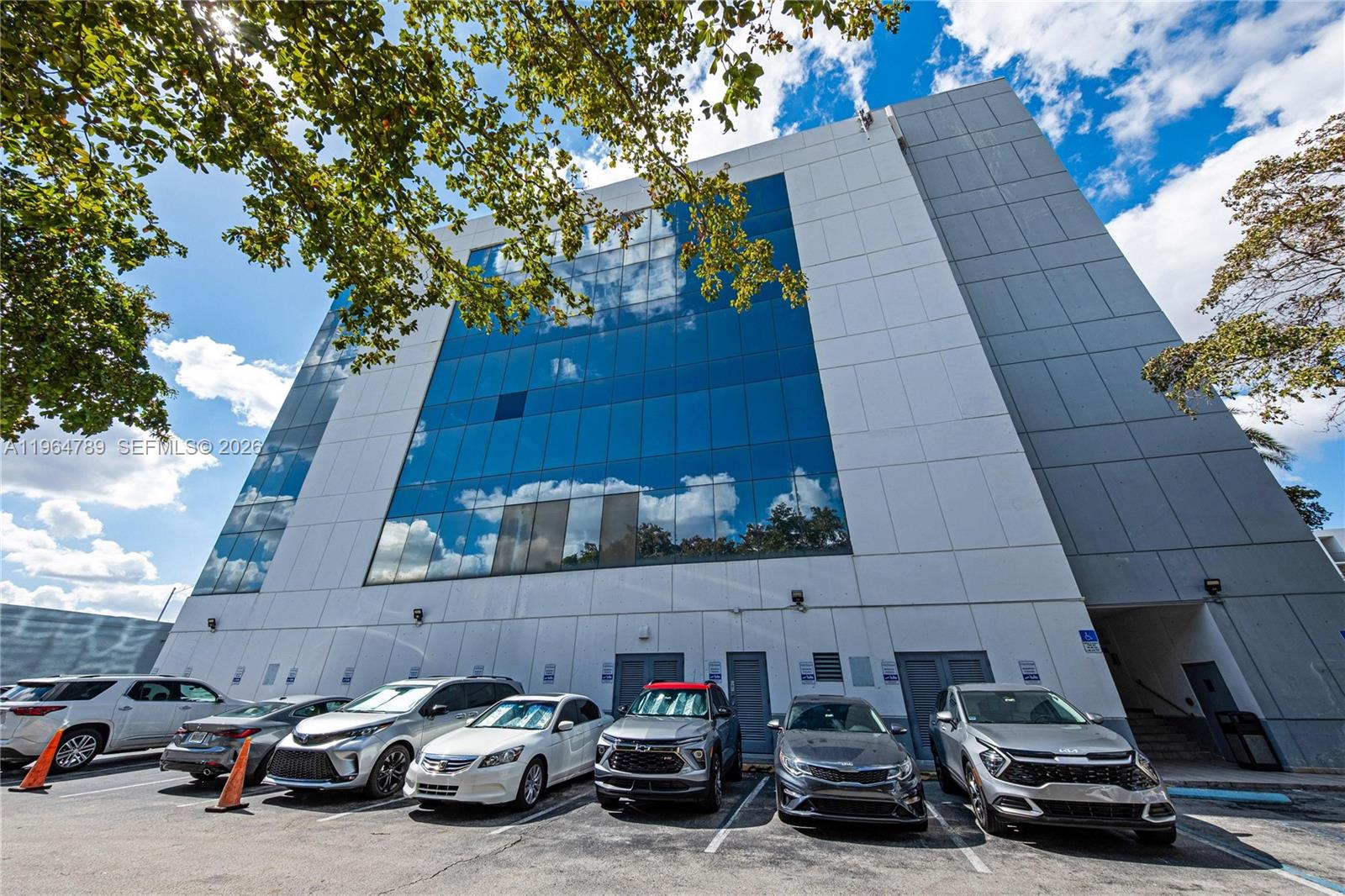 A low-angle exterior view of a modern office building with a glass facade and parking — 4445 W 16th Ave # 600, Hialeah FL 33012, HIALEAH, FL