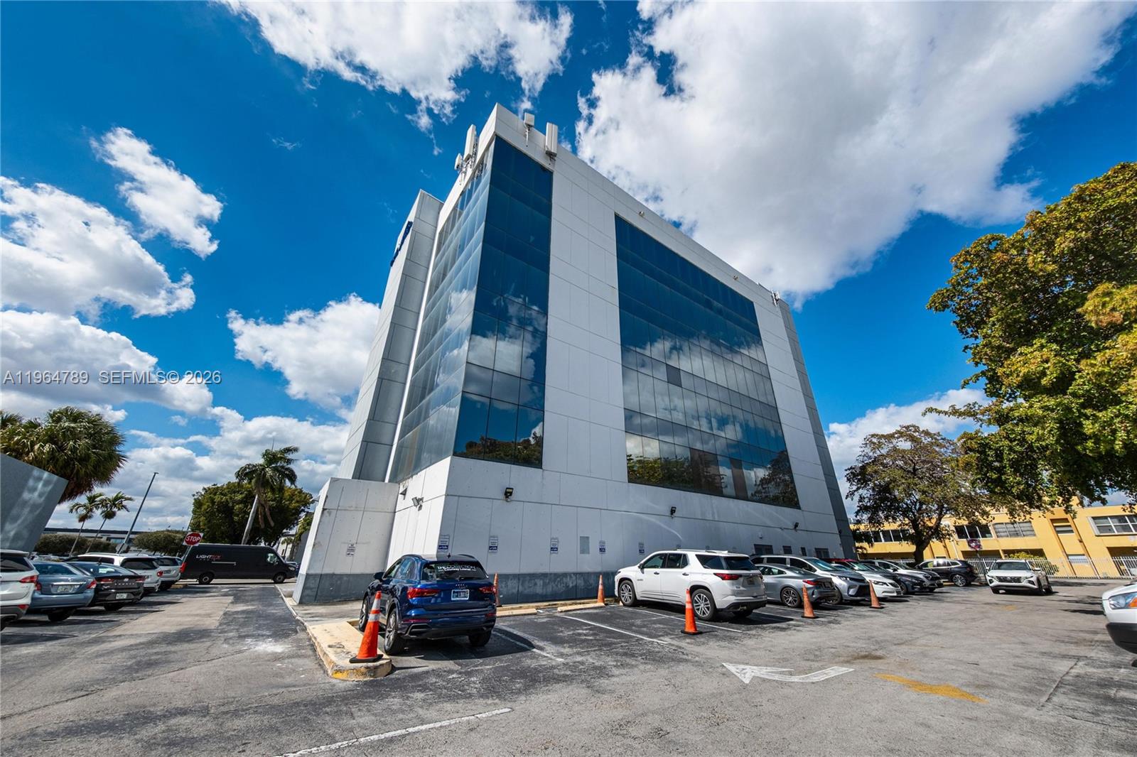 A multi-story office building with a glass facade stands above a paved parking lot — 4445 W 16th Ave # 600, Hialeah FL 33012, HIALEAH, FL