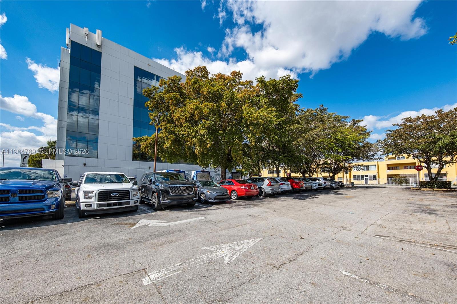 A parking lot with several parked cars sits in front of a modern office building — 4445 W 16th Ave # 600, Hialeah FL 33012, HIALEAH, FL