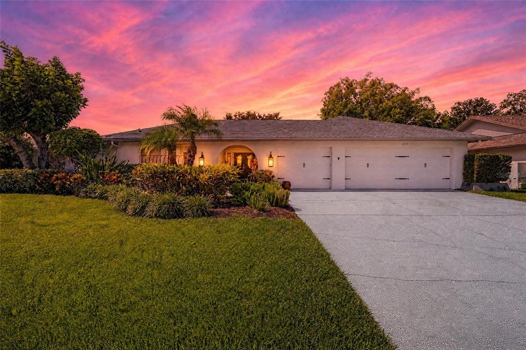 A single-story house with a two-car garage and landscaped front yard under a sunset sky — 2717 REDFORD COURT E, CLEARWATER, FL