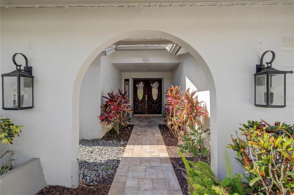 A stone walkway leads through an arched entryway to double front doors with decorative glass — 2717 REDFORD COURT E, CLEARWATER, FL