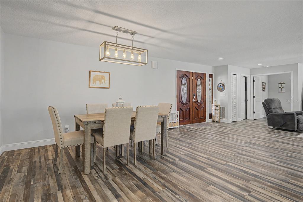 A dining area features a wooden table with upholstered chairs, a rectangular chandelier, and wood-look flooring — 2717 REDFORD COURT E, CLEARWATER, FL