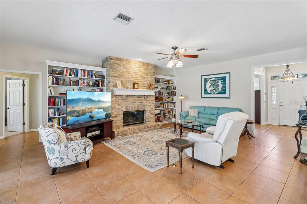 A living room features a brick fireplace, built-in bookshelves, tile flooring, and comfortable seating — 1616 REGAL COVE COURT, KISSIMMEE, FL