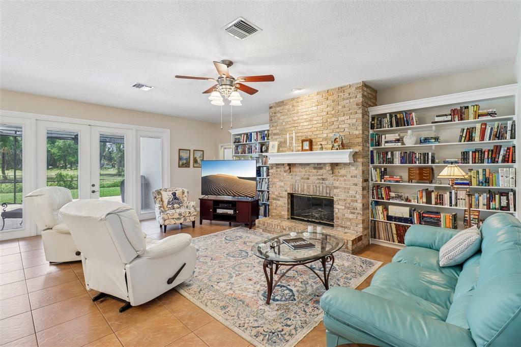 A living room features a brick fireplace, built-in bookshelves, a television, and tile flooring — 1616 REGAL COVE COURT, KISSIMMEE, FL