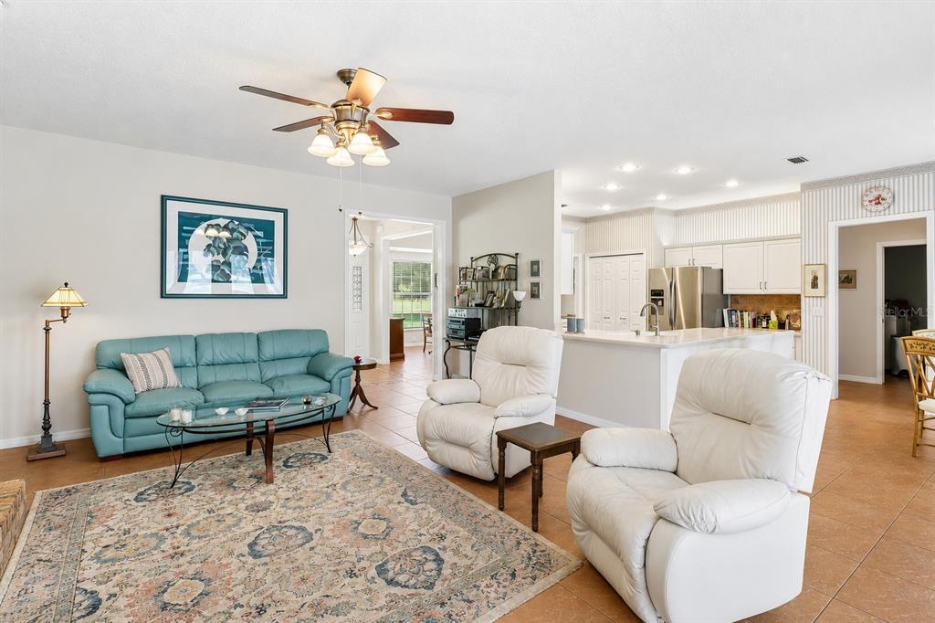 A living room with a teal sofa, two white recliners, and an open kitchen area — 1616 REGAL COVE COURT, KISSIMMEE, FL
