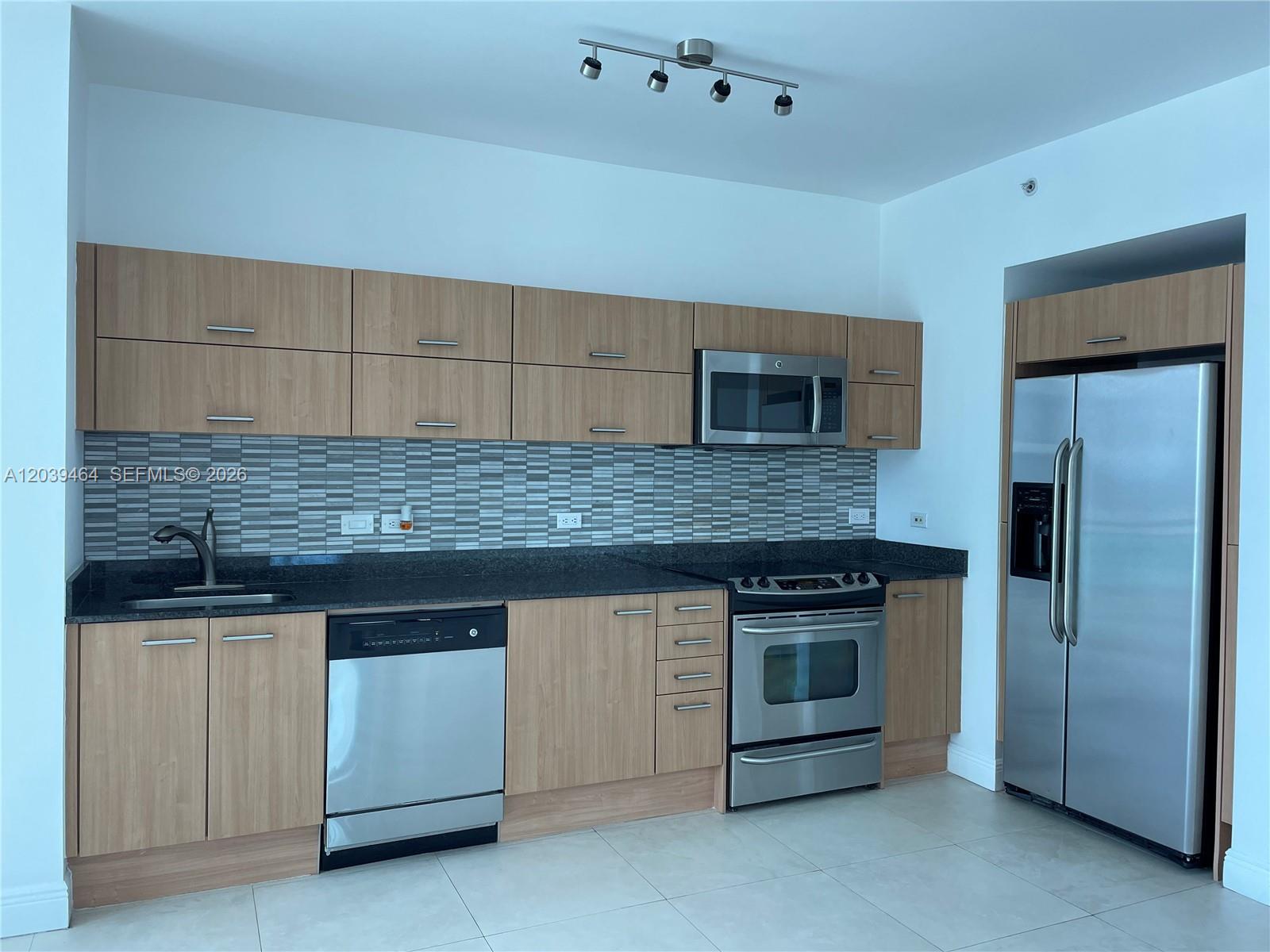 A modern kitchen features light wood cabinets, stainless steel appliances, and a gray tiled backsplash — 350 S Miami Ave # 1913, Miami FL 33130, MIAMI, FL