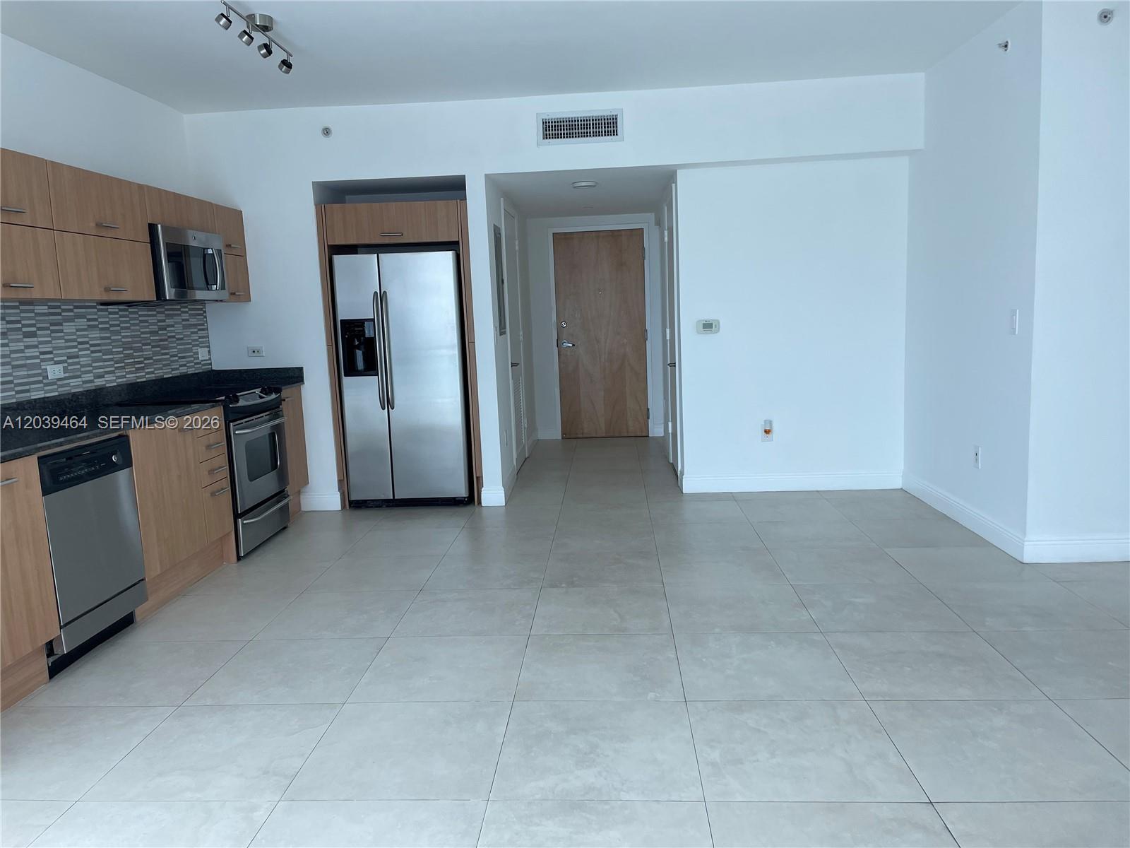 A modern kitchen with stainless steel appliances and light wood cabinets opens to a tiled area — 350 S Miami Ave # 1913, Miami FL 33130, MIAMI, FL