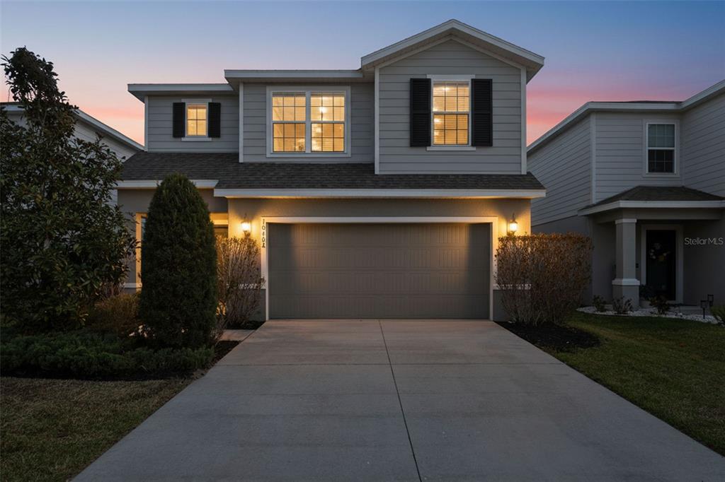 A two-story gray house with a two-car garage and a concrete driveway at dusk — 10402 HAWKS LANDING DRIVE, LAND O LAKES, FL