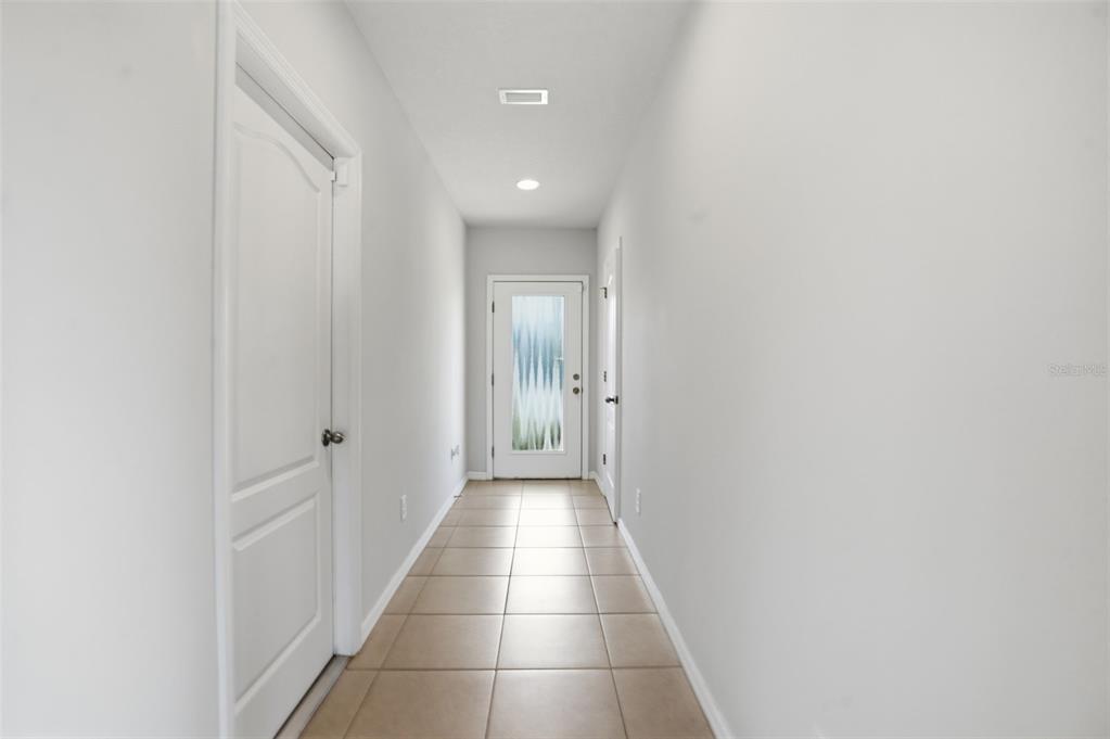 A hallway with light-colored walls, tile flooring, and a door with a frosted glass panel — 10402 HAWKS LANDING DRIVE, LAND O LAKES, FL