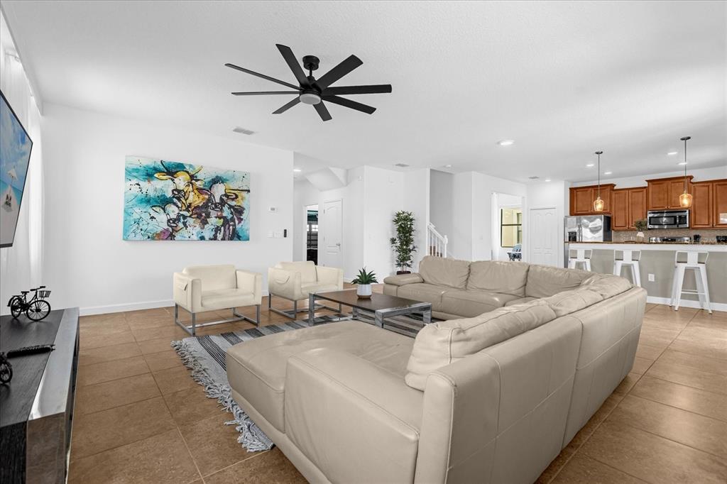 A spacious open-concept living room features a large sectional sofa, two armchairs, and tile flooring — 1483 ROLLING FAIRWAY DRIVE, CHAMPIONS GATE, FL