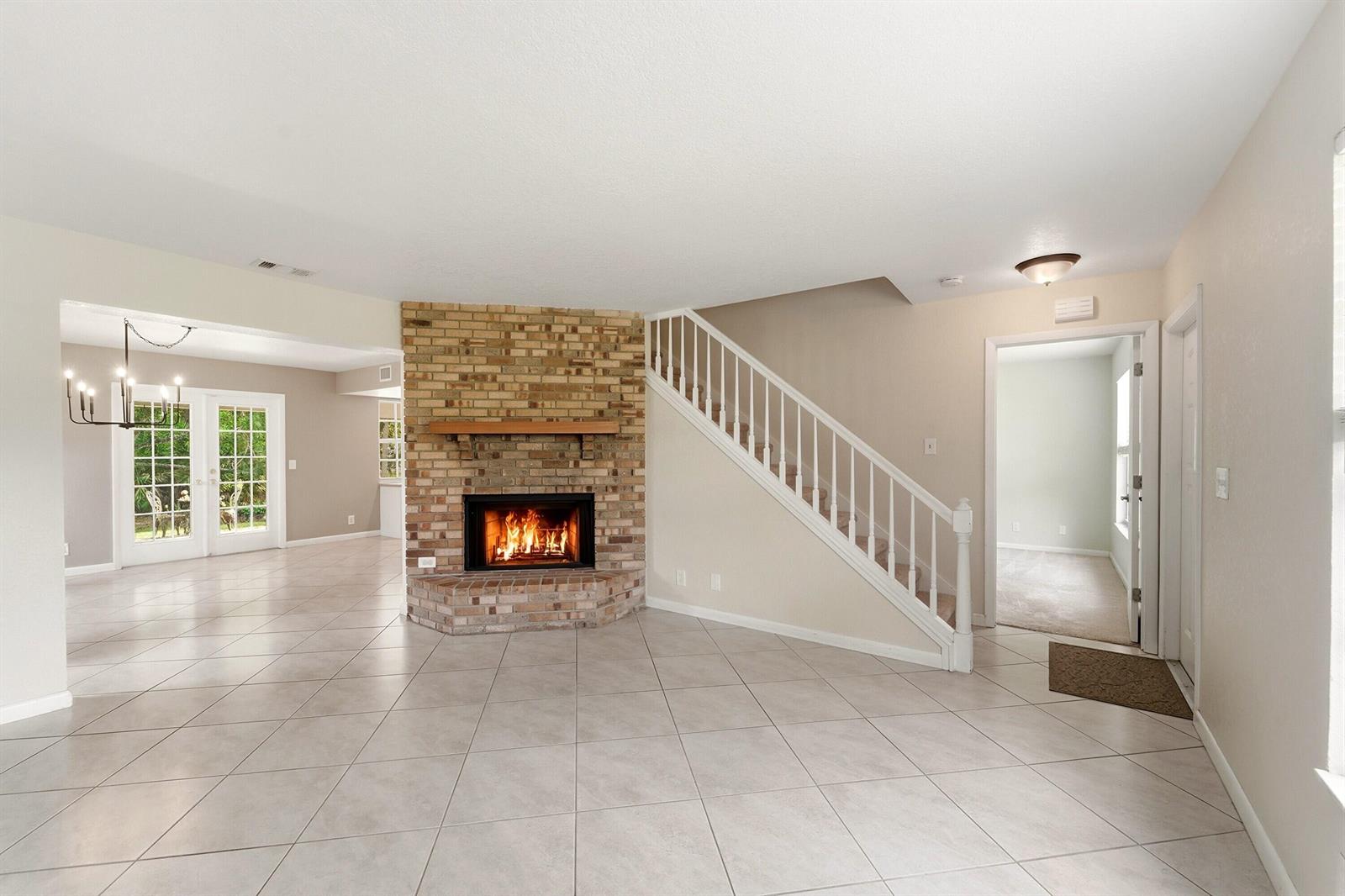 A living room features a brick fireplace, white staircase, and light-colored tile flooring — 16317 Glasgow Drive E, FL 33470, FL