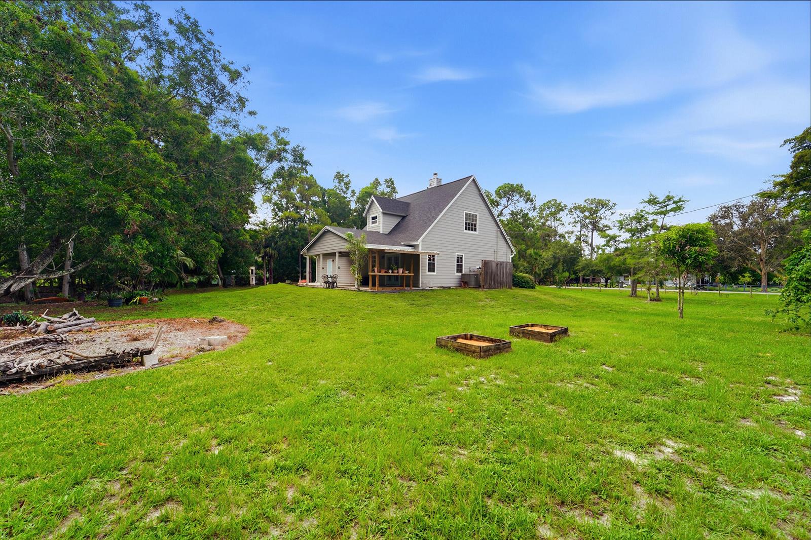 A gray two-story house sits on a large grassy lot with two raised garden beds — 16317 Glasgow Drive E, FL 33470, FL