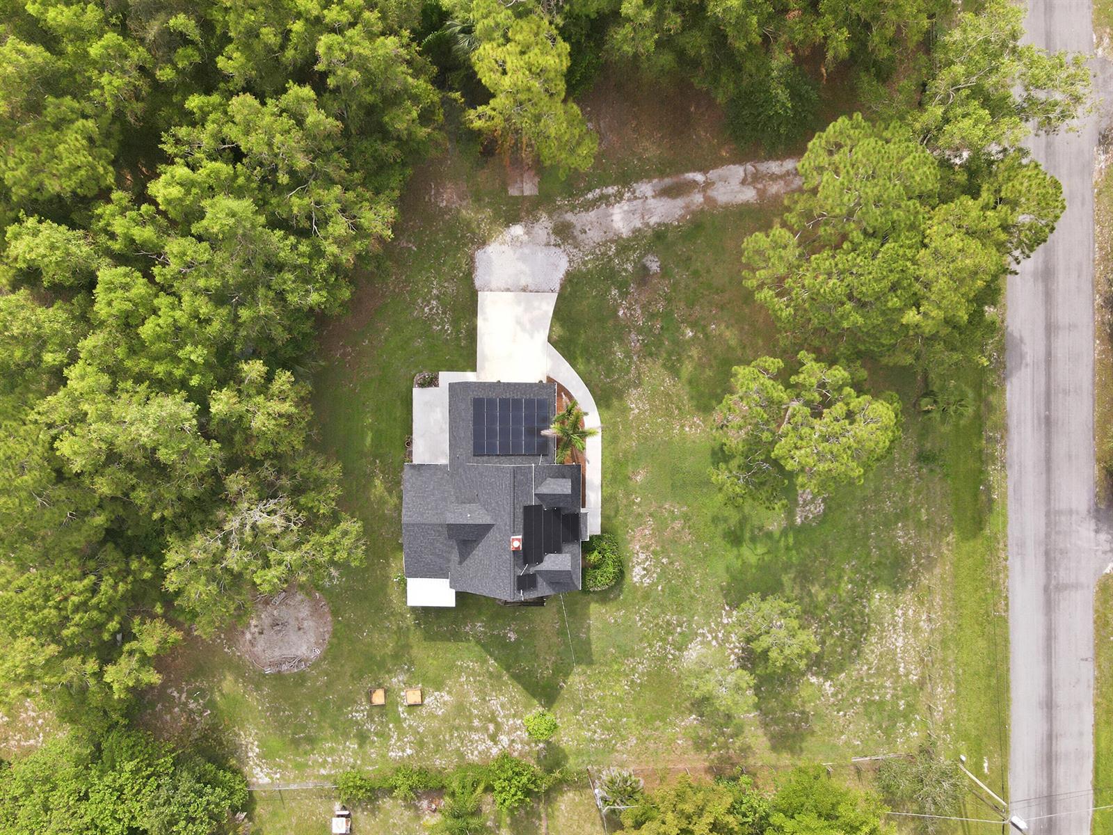 An aerial view shows a house with solar panels on its roof surrounded by trees — 16317 Glasgow Drive E, FL 33470, FL