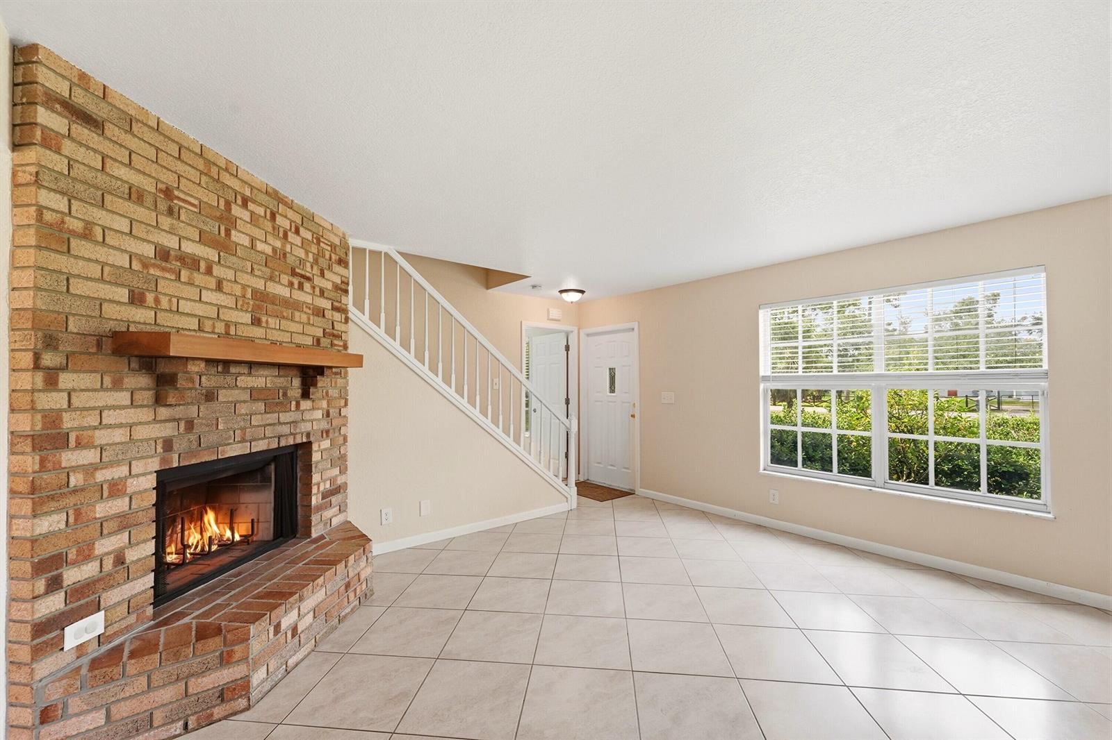 A living room features a brick fireplace, tile flooring, a staircase, and a large window — 16317 Glasgow Drive E, FL 33470, FL