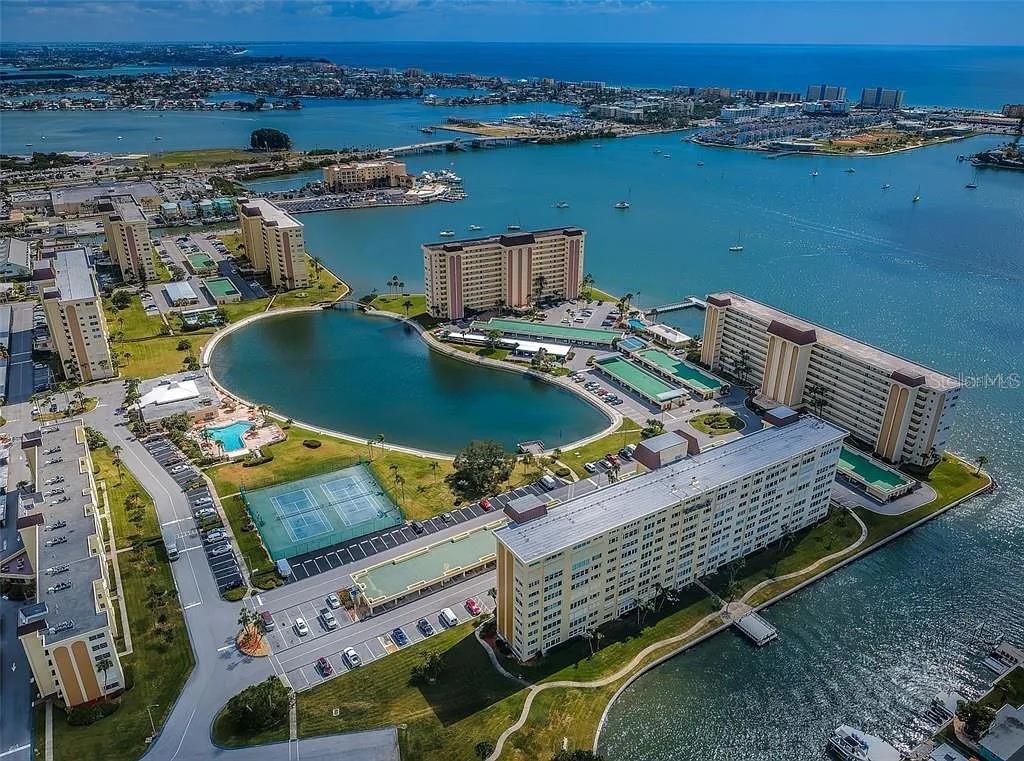 An aerial view shows a waterfront apartment complex with a central lake and tennis courts — 4575 COVE CIRCLE UNIT 703, ST PETERSBURG, FL