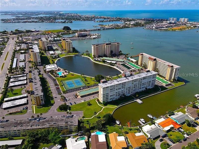 Aerial view of a waterfront apartment complex with a central lake and tennis courts — 4575 COVE CIRCLE UNIT 703, ST PETERSBURG, FL