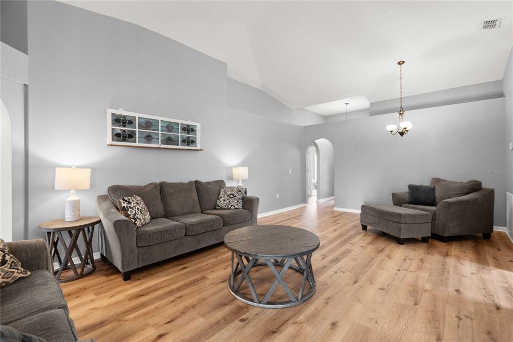 A living room features gray walls, wood-look flooring, a vaulted ceiling, and gray upholstered furniture — 14423 FINSBURY DRIVE, SPRING HILL, FL