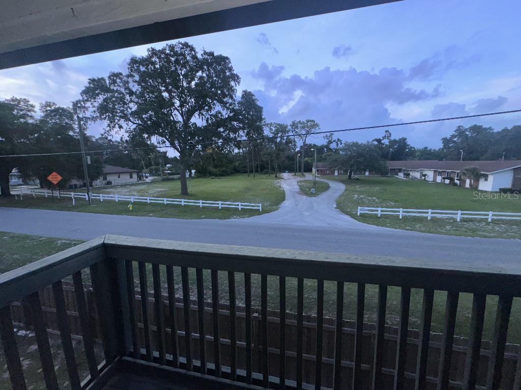 A view from a wooden balcony overlooking a grassy lot, a road, and nearby buildings — 12406 HIBISCUS OAK PLACE UNIT 202, TAMPA, FL