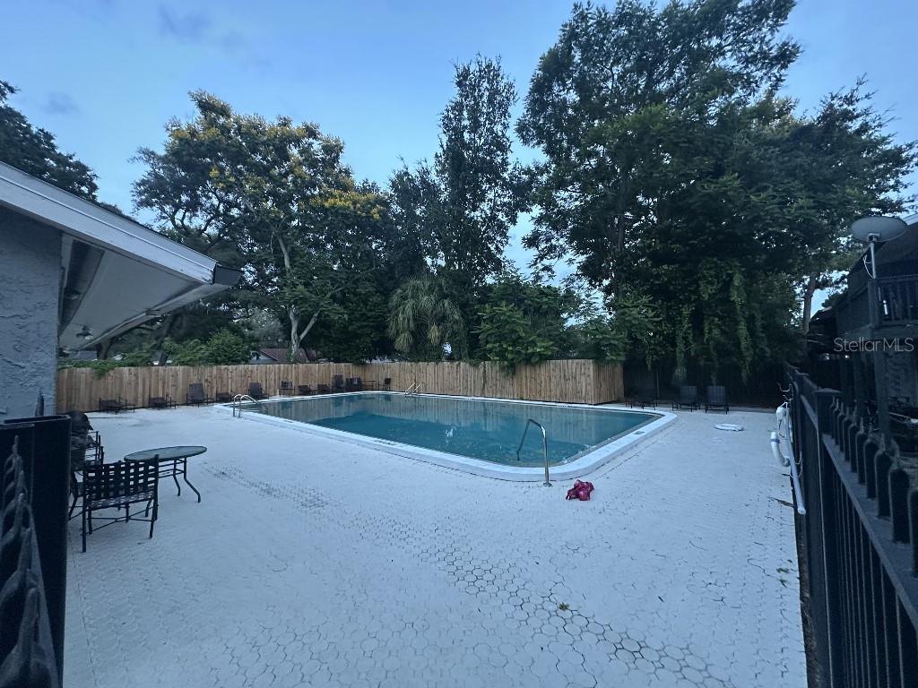 A rectangular swimming pool is surrounded by a white patio and a wooden fence — 12406 HIBISCUS OAK PLACE UNIT 202, TAMPA, FL