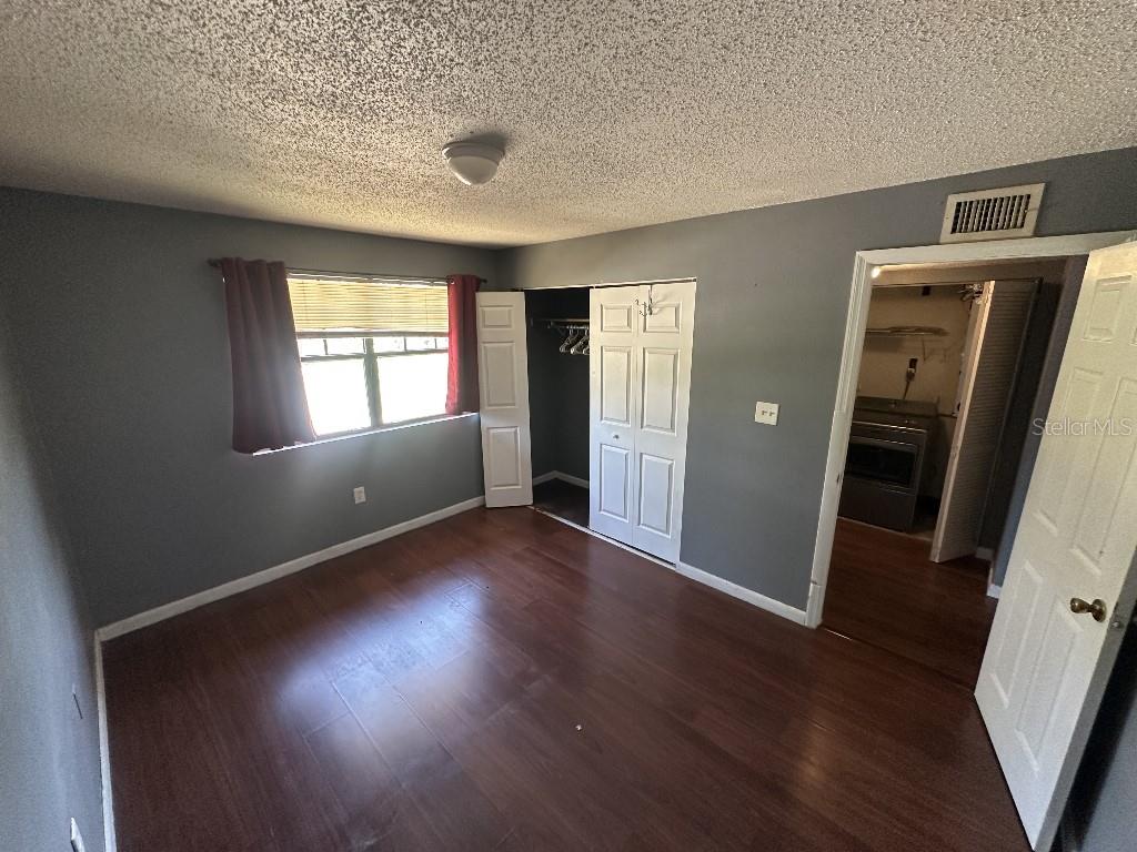 A bedroom with gray walls, wood-look flooring, a window with curtains, and an open closet — 12406 HIBISCUS OAK PLACE UNIT 202, TAMPA, FL