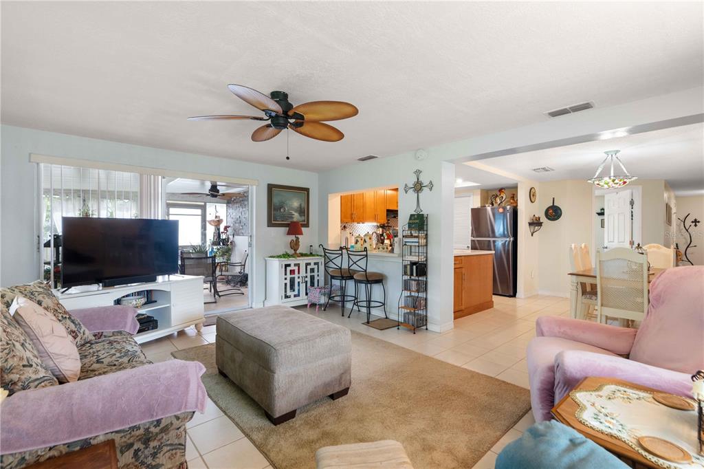 A living room with a ceiling fan, beige rug, television, and an open kitchen beyond — 8216 CAVALRY DRIVE, HUDSON, FL
