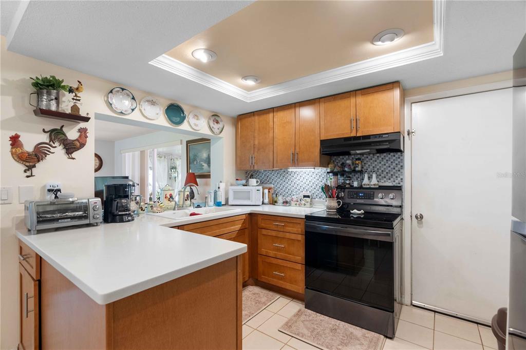 A kitchen features wood cabinets, white countertops, a black stove, and a tiled backsplash — 8216 CAVALRY DRIVE, HUDSON, FL