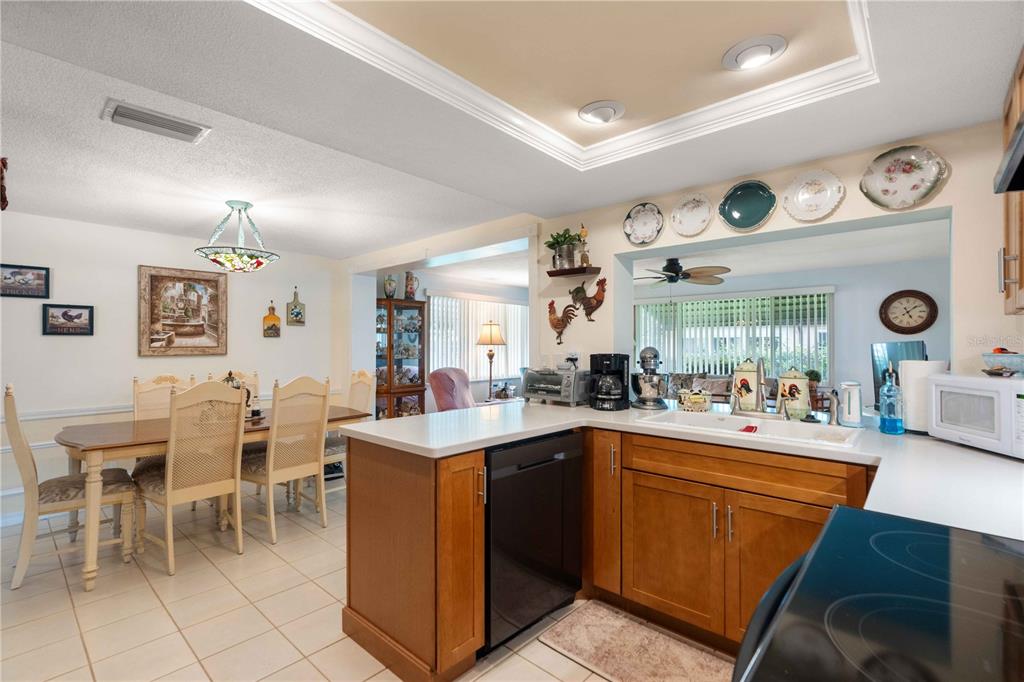 A kitchen with wood cabinets and white countertops opens to a dining area with tile floors — 8216 CAVALRY DRIVE, HUDSON, FL