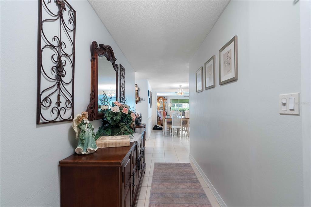 A hallway with a wooden console table, wall decor, and a runner leads to a dining area — 8216 CAVALRY DRIVE, HUDSON, FL