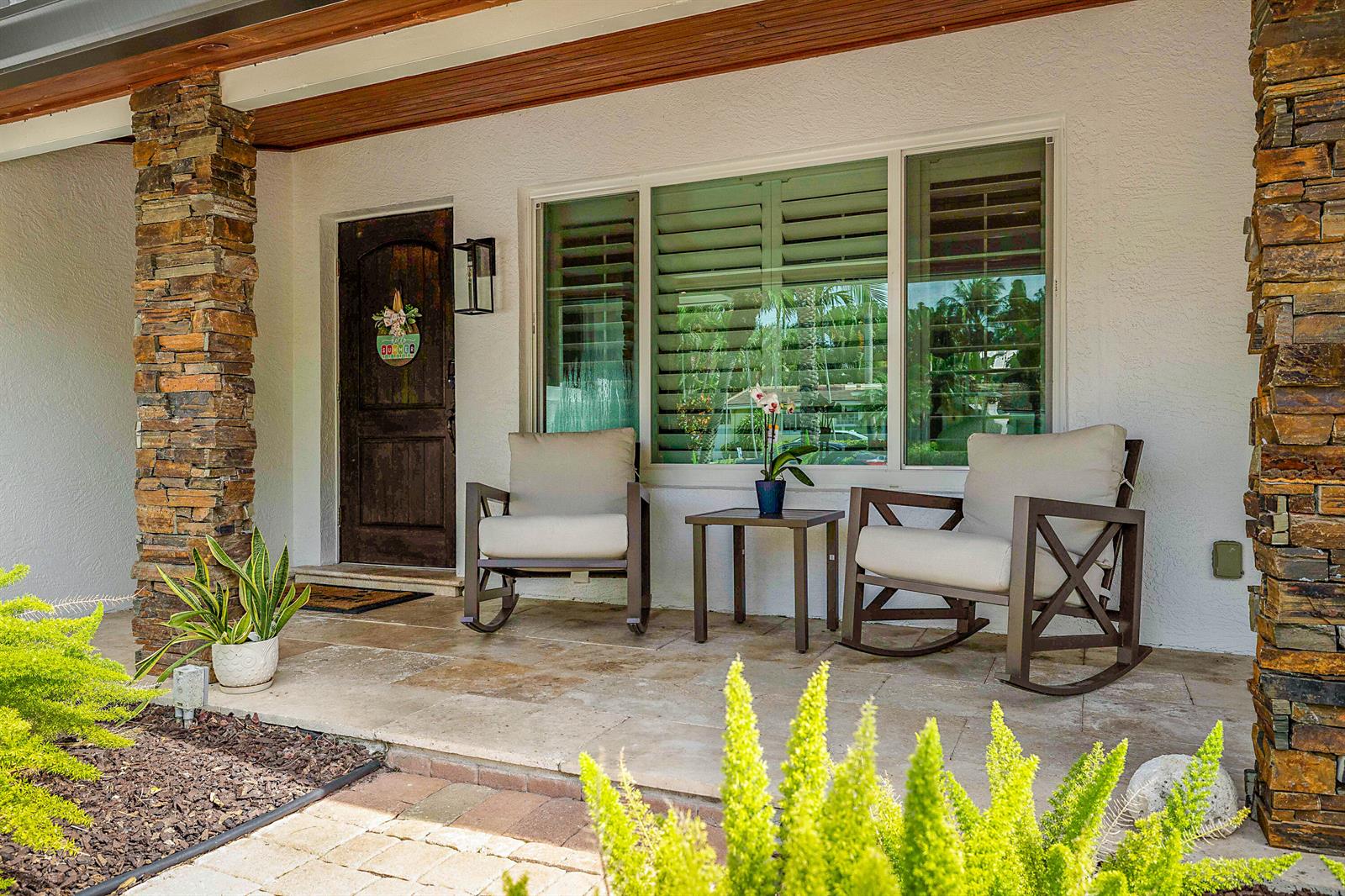 A covered front porch features stone pillars, two rocking chairs, a small table, and a door — 2620 NE 53rd Street, Lighthouse Point FL 33064, LIGHTHOUSE POINT, FL