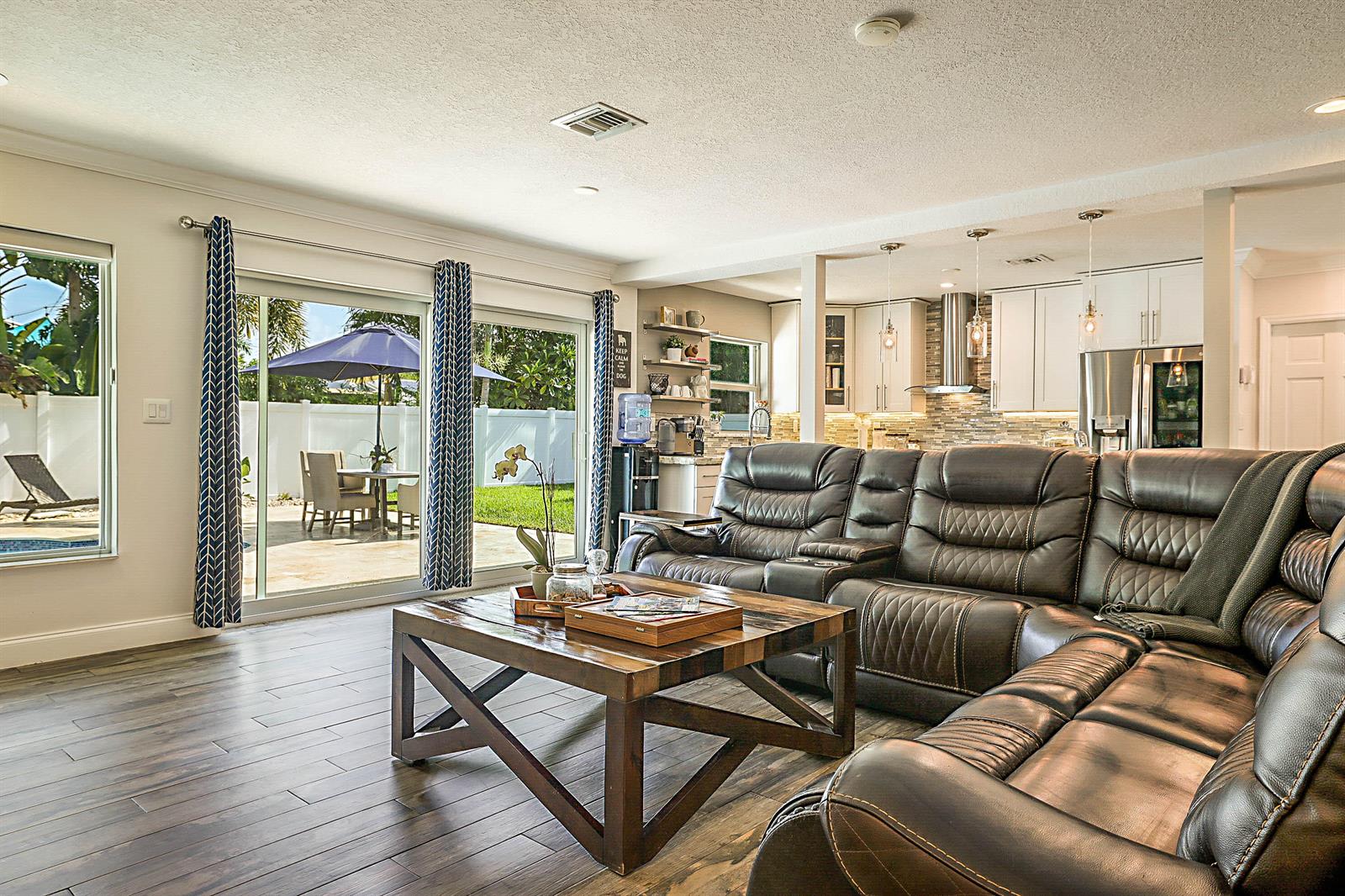 A living room with a dark leather sectional, wooden coffee table, and sliding glass patio doors — 2620 NE 53rd Street, Lighthouse Point FL 33064, LIGHTHOUSE POINT, FL