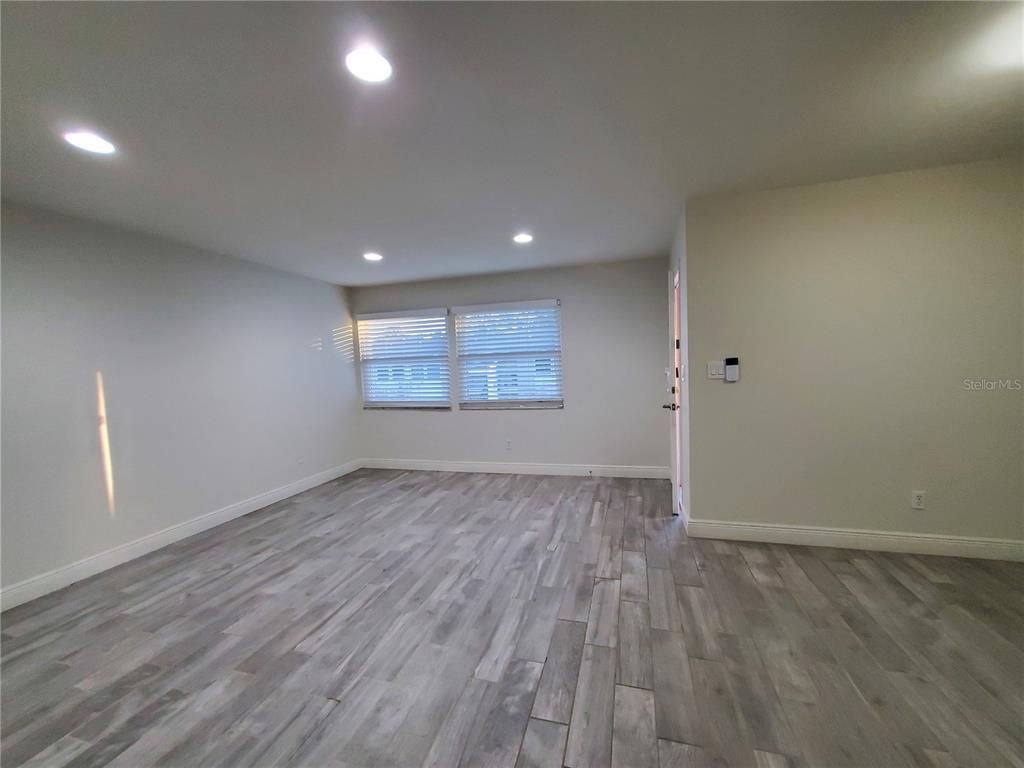 An empty room features light gray wood-look flooring, recessed lighting, and two windows with blinds — 3107 W HORATIO STREET UNIT B22, TAMPA, FL