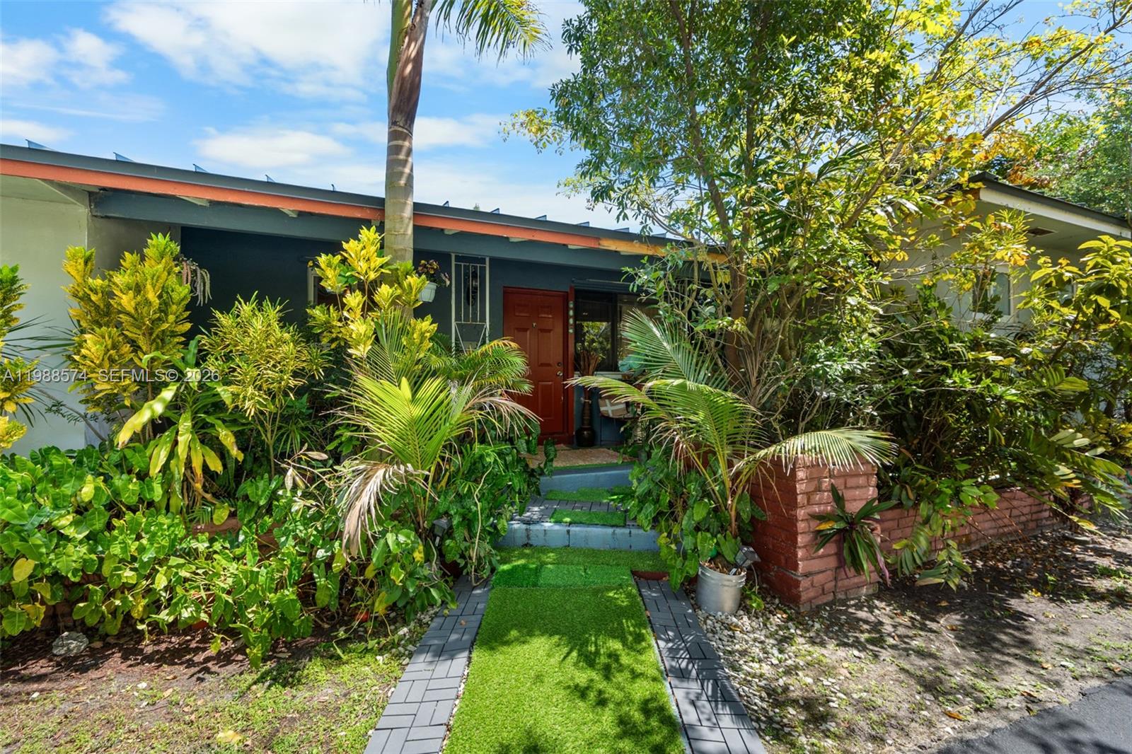 A front view of a house with a red door, lush landscaping, and a paved walkway — 6005 SW 64th Pl, South Miami FL 33143, SOUTH MIAMI, FL