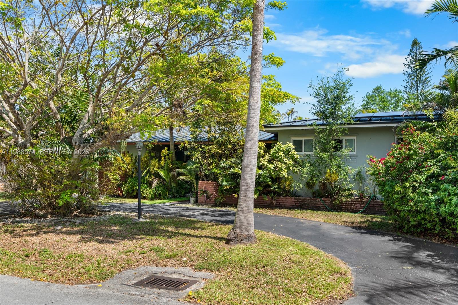 A single-story house with a curved driveway is partially obscured by trees and lush landscaping — 6005 SW 64th Pl, South Miami FL 33143, SOUTH MIAMI, FL