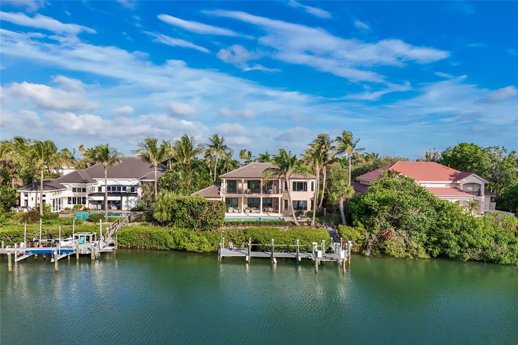 Three waterfront houses with private docks sit along a canal under a blue sky — 65 LIGHTHOUSE POINT DRIVE, LONGBOAT KEY, FL