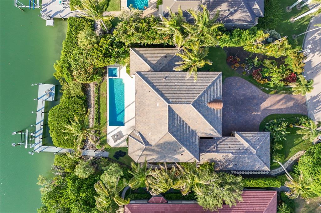 An aerial view shows a waterfront house with a swimming pool, dock, and paved driveway — 65 LIGHTHOUSE POINT DRIVE, LONGBOAT KEY, FL