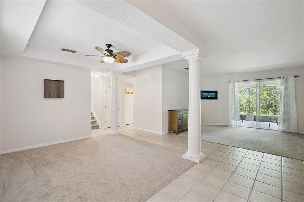 A living area with carpeted floors, white columns, a ceiling fan, and sliding glass doors — 2589 CORBYTON COURT, ORLANDO, FL