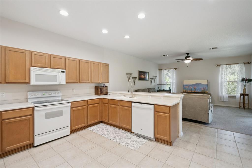 A kitchen with light wood cabinets and white appliances opens into a carpeted living area — 2589 CORBYTON COURT, ORLANDO, FL