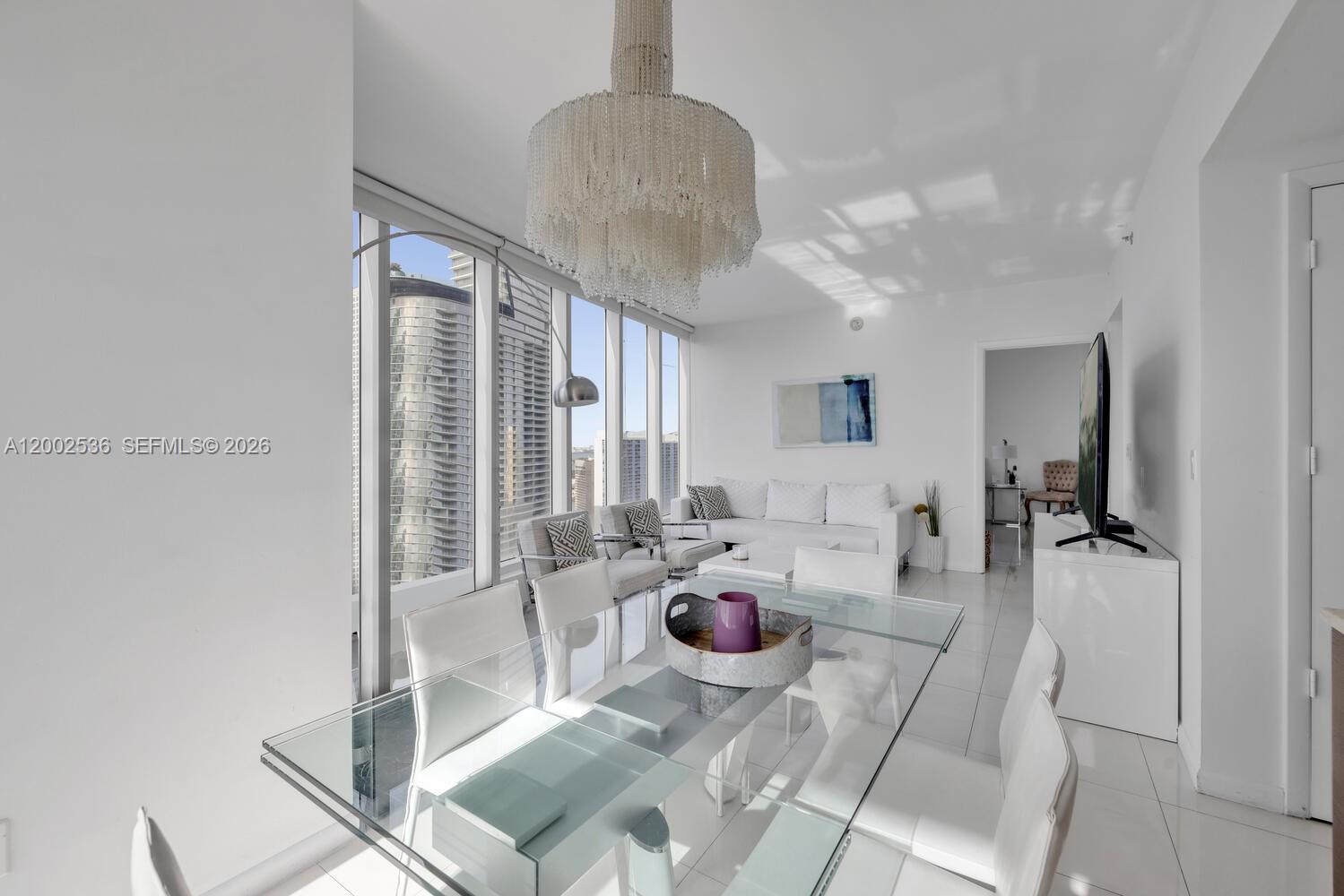 A bright dining and living area features a glass table, chandelier, and floor-to-ceiling windows — 485 Brickell Ave # 4104, Miami FL 33131, MIAMI, FL