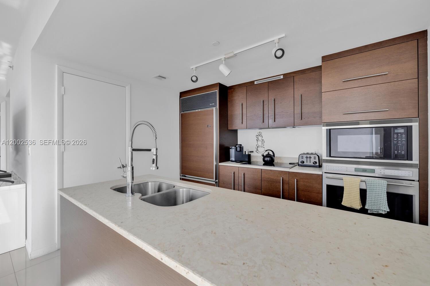A modern kitchen features dark wood cabinetry, a stone island countertop, and stainless steel appliances — 485 Brickell Ave # 4104, Miami FL 33131, MIAMI, FL
