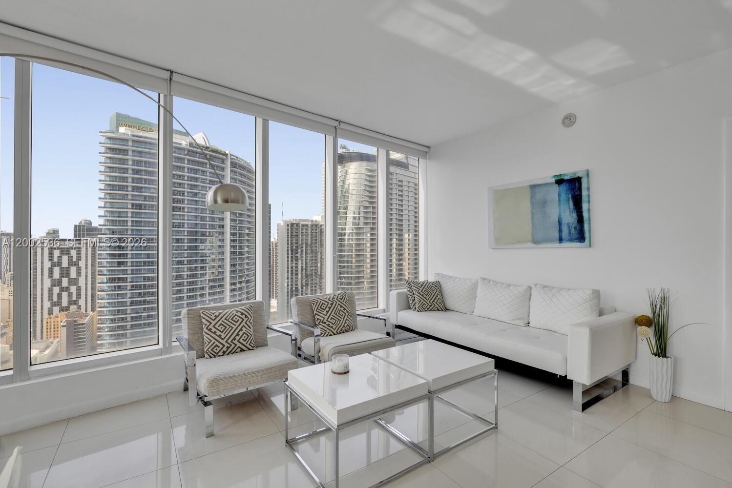 A modern living room features a white sofa, two armchairs, and floor-to-ceiling windows with city views — 485 Brickell Ave # 4104, Miami FL 33131, MIAMI, FL