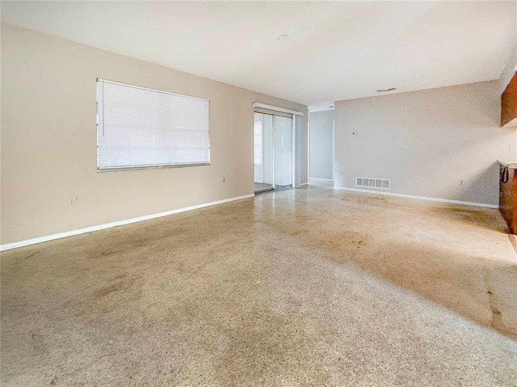An empty living room features beige walls, a large window with blinds, and concrete flooring — 4417 PARNELL DRIVE, SARASOTA, FL