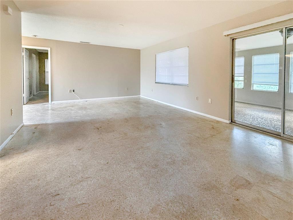 An empty living room features beige walls, a sliding glass door, and concrete flooring — 4417 PARNELL DRIVE, SARASOTA, FL