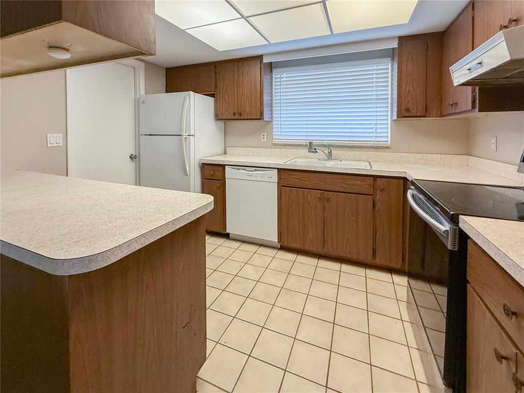 A kitchen features wood cabinets, white appliances, a tiled floor, and a breakfast bar — 4417 PARNELL DRIVE, SARASOTA, FL