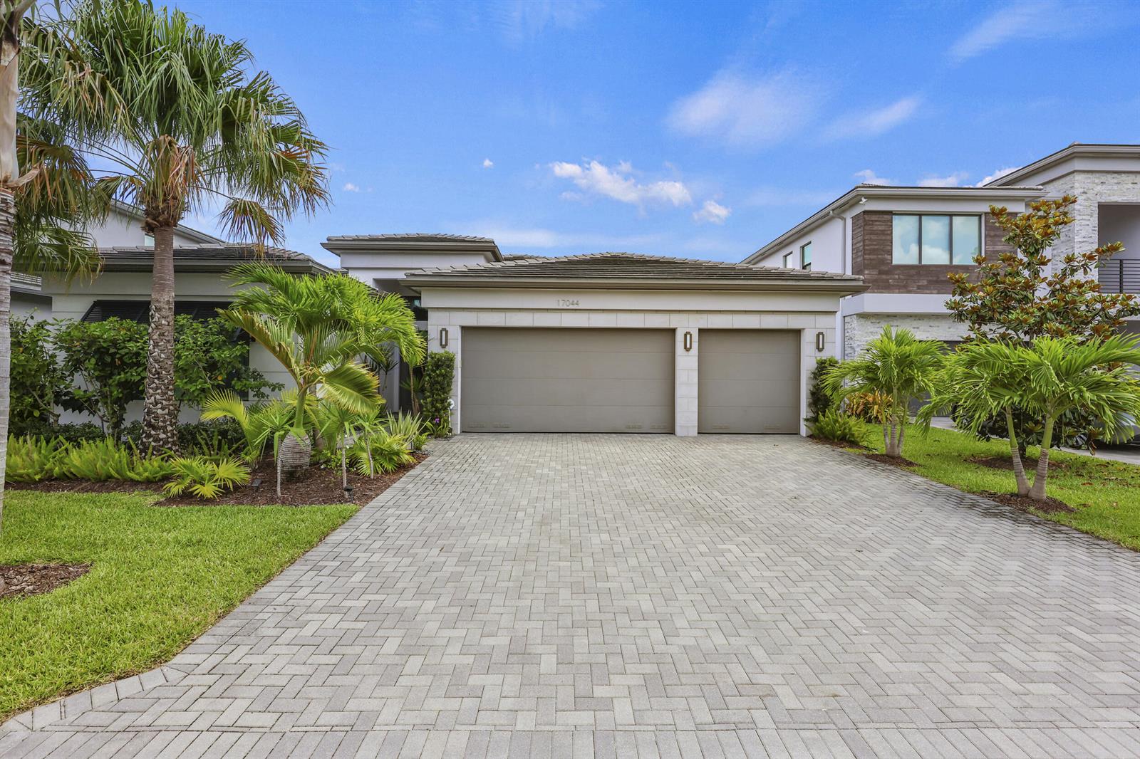 A single-story house features a three-car garage, a paved driveway, and tropical landscaping — 17044 Watersprite Lakes Road, Boca Raton FL 33496, BOCA RATON, FL