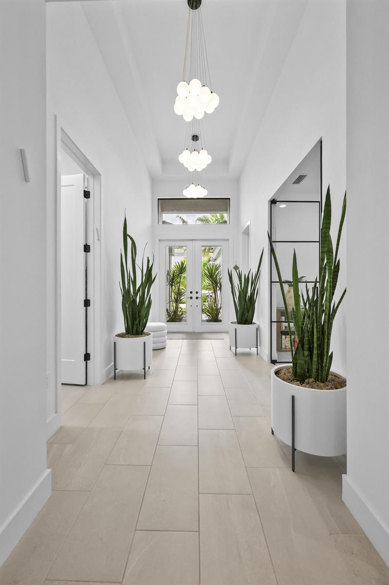 A bright hallway features white walls, light tile flooring, three globe chandeliers, and potted plants — 17044 Watersprite Lakes Road, Boca Raton FL 33496, BOCA RATON, FL