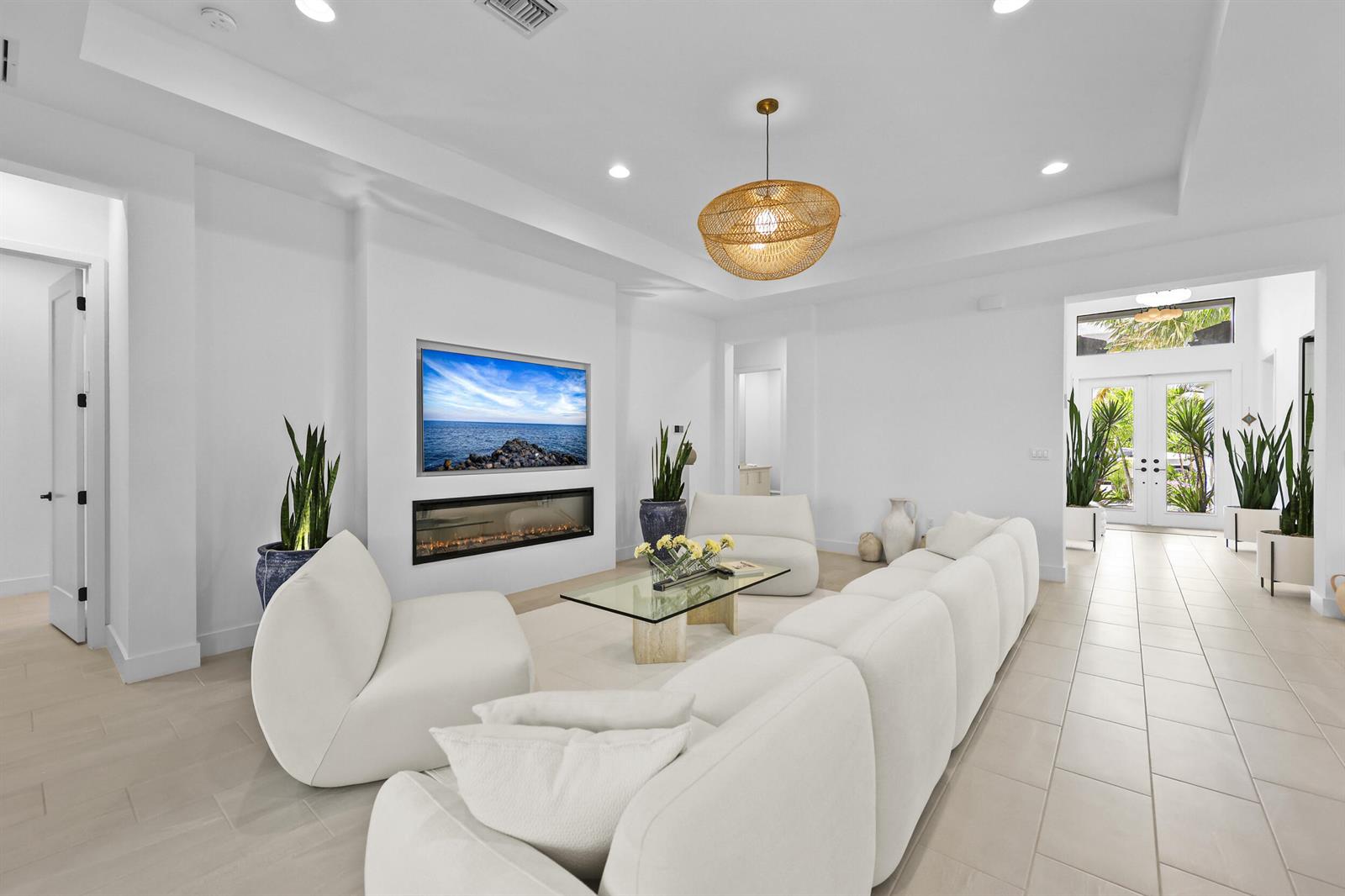 A bright living room features white furniture, a fireplace, a wall-mounted television, and tile flooring — 17044 Watersprite Lakes Road, Boca Raton FL 33496, BOCA RATON, FL