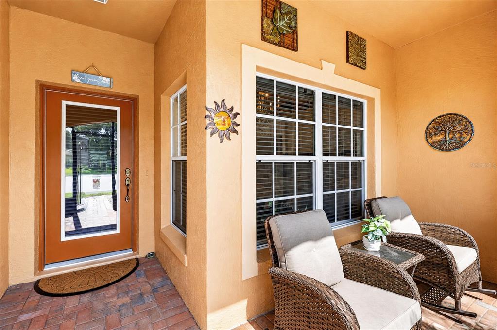 A covered porch features a brown door, two wicker chairs, and decorative wall art — 4188 ABERDEEN LANE, LAKE WALES, FL