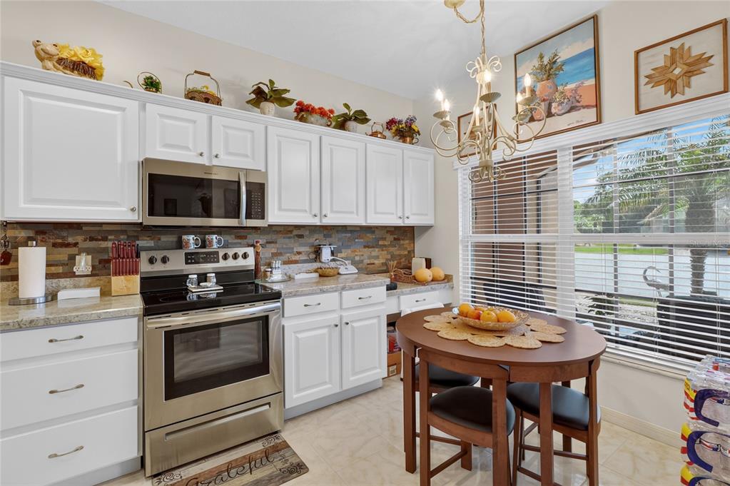 A kitchen features white cabinets, stainless steel appliances, a stone backsplash, and a dining table — 4188 ABERDEEN LANE, LAKE WALES, FL