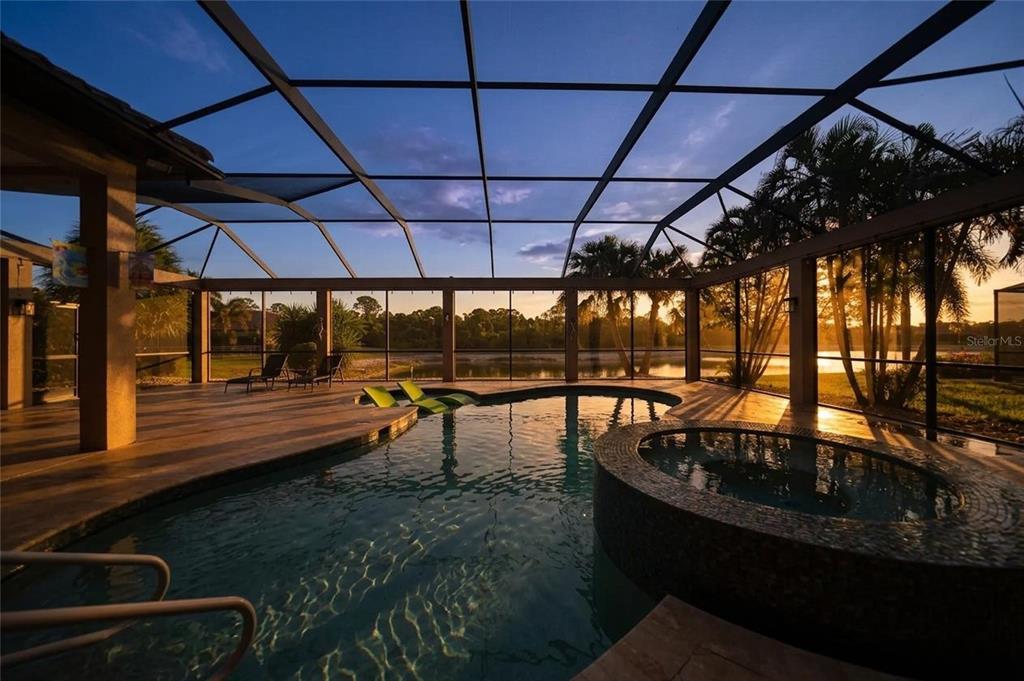 A screened-in pool and hot tub area overlooking a lake at sunset — 13220 CAMPANILE COURT, VENICE, FL
