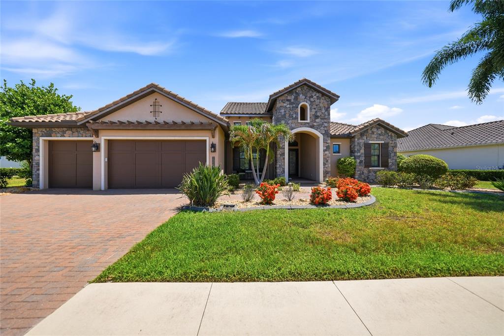 A single-story house with a stone facade, a three-car garage, and a landscaped front yard — 13220 CAMPANILE COURT, VENICE, FL